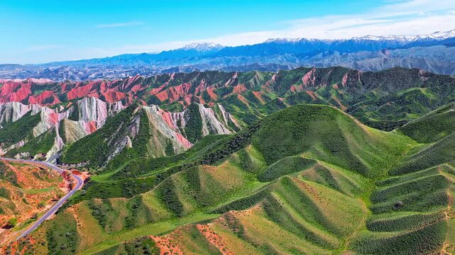 Aerial view of colorful striped rock formations and a winding road in a valley along the S101 highway in Xinjiang, China.