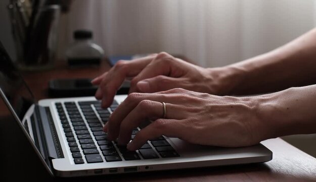 Close-up of Hands Typing on a Laptop at a Wooden Desk, Working from Home
木製デスクでノートパソコンをタイピングする手元のクローズアップ　在宅ワークのイメージ