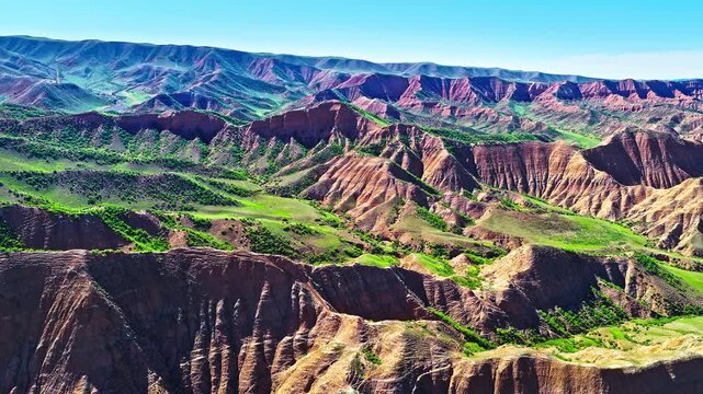 Aerial view of a vast eroded canyon landscape with red clay ridges and green valleys along the S101 highway in Xinjiang, China.