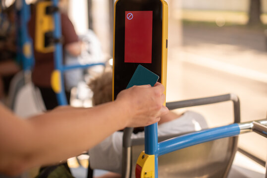 A hand holding a contactless card approaches a bus fare reader. The scene captures a public transport setting with a focus on modern payment technology.