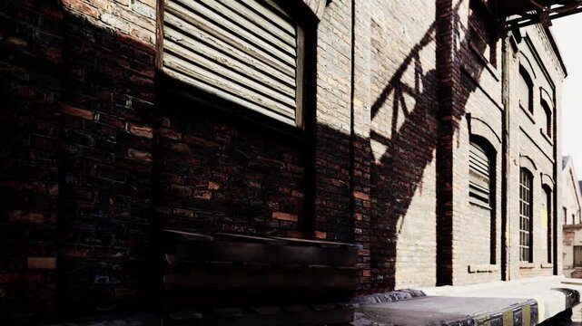 Sunlight creates sharp shadows across the textured red brick walls of this old industrial warehouse building while wooden pallets sit stacked on the concrete platform near the loading dock area