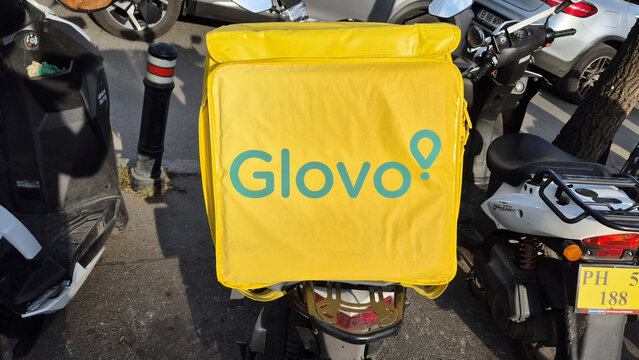 Bright yellow Glovo delivery backpack mounted on a scooter parked on a city street. Picture taken on October 15, 2026 in Bucharest, Romania.