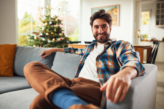 Smiling young man relaxing on sofa in living room near christmas tree