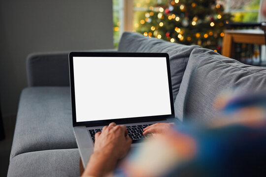 Man typing on laptop with blank screen near christmas tree - mockup