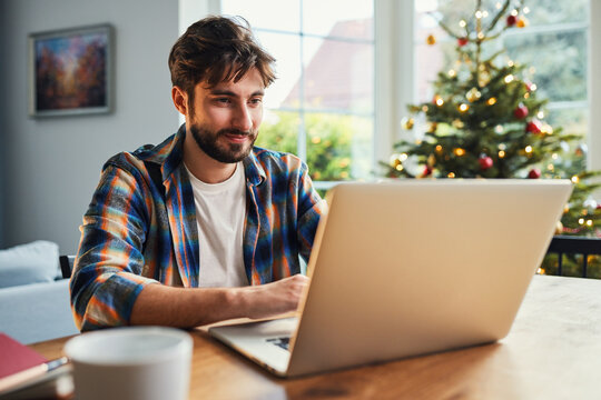 Young man working on laptop at home near christmas tree