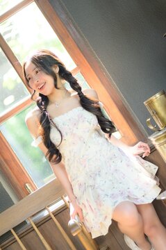 Joyful young woman sitting on window sill in bright daylight, smiling, casual dress, natural light, home interior, relaxed mood, cozy atmosphere, soft shadows, cheerful expression, leisure moment
