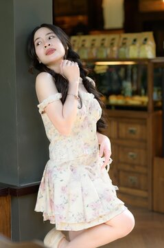 Young woman with long dark hair in soft floral dress leaning against wall indoors