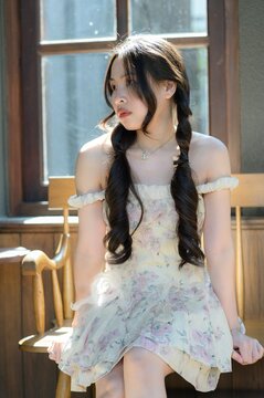 Young woman with long dark hair and braids sitting near a window in sunlight