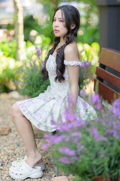 Young woman with long dark hair sitting on garden bench surrounded by colorful flowers