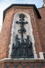 A striking religious bas-relief depicting the crucifixion, protected by mesh, adorns the robust red brick wall of St. Mary's Basilica in Krakow, Poland. © Danica Chang