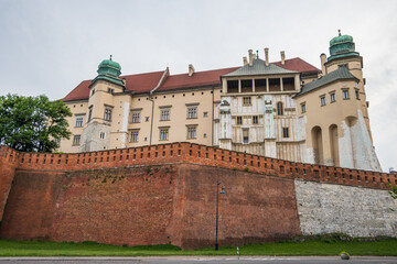 Wawel Royal Castle and Cathedral complex features beige plaster, red roofs, green domes and rises above formidable red brick and grey stone defensive walls in Krakow, Poland. © Danica Chang
