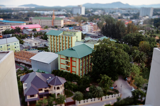 Aerial tilt-shift photograph showing colorful residential buildings, tree-lined streets and mixed urban development in a small city, conveying scale, calm neighborhood life and architectural variety.