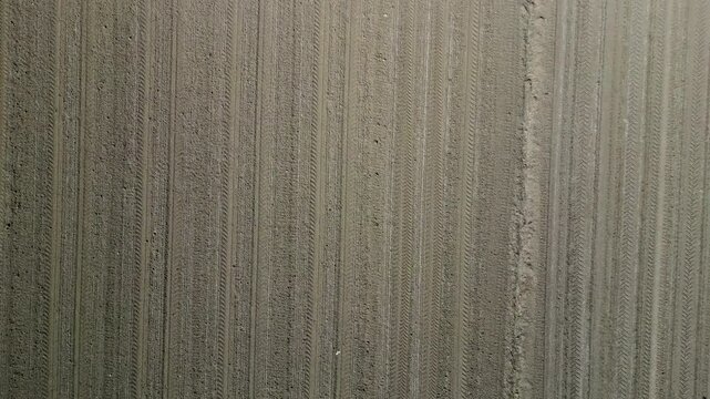 Top-down aerial drone view of plowed agricultural field with tractor tire tracks, geometric diagonal lines and textured brown soil, abstract farmland background for farming and agriculture in Italy