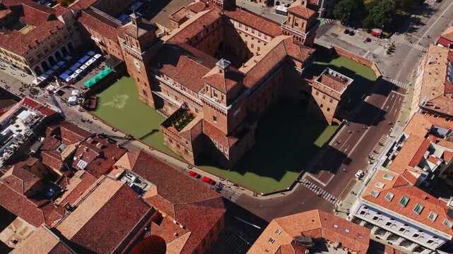 Aerial drone view of Castello Estense in Ferrara, Italy, showcasing the historic Renaissance castle, moat, towers, red rooftops, and surrounding city center.