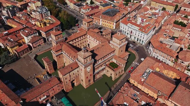 Aerial drone view of Castello Estense in Ferrara, Italy, showcasing the historic Renaissance castle, moat, towers, red rooftops, and surrounding city center.