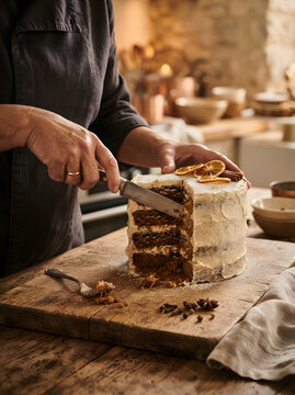 Chef slicing a frosted layered cake on a wooden board