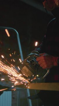 Man working at factory cuts metal with a grinder. Male at a construction site cuts off piece, bright flying sparks and particles of material fly. Guy Industrial worker use angle grinder cutting metal
