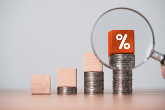 Interest rate growth and financial investment analysis concept with rising coin stacks and magnifying glass highlight a percentage symbol for savings and investment returns the highest profit.
