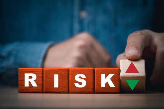 Business risk assess management concept with wooden blocks spelling RISK and a hand holding up and down arrows for financial uncertainty, risk control and strategic decisions.