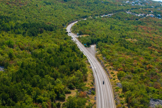 Elevated drone perspective of a two-lane road running through dense green vegetation and rocky karst terrain