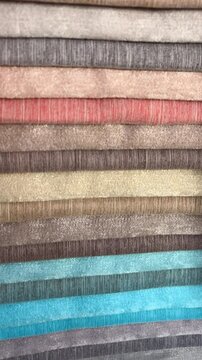 Vertical orientation slow motion close up shot of upholstery fabric samples in various colors in a textile store
