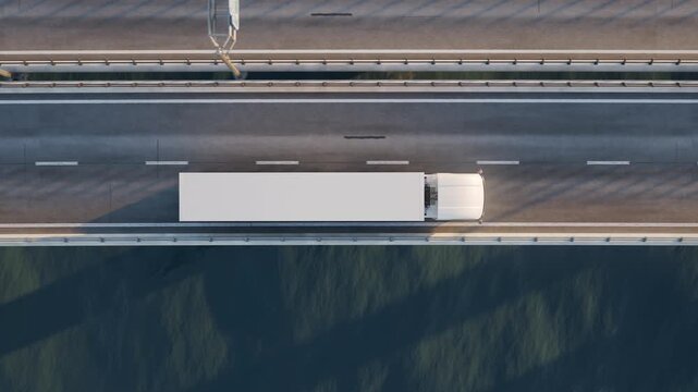 A directly overhead camera tracks a white semi truck moving left to right across a long bridge over water, showing the trailer and lane markings from above.