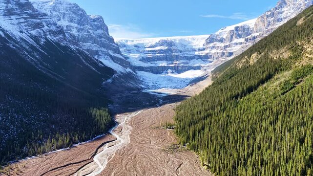 Aerial drone view of a glacier and a winding river valley between forested slopes, Jasper National Park, Canada.