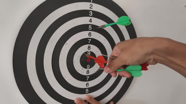 Slow motion close-up of a hand gripping and removing a red dart from a black and white numbered dartboard, revealing the target rings and red bullseye.