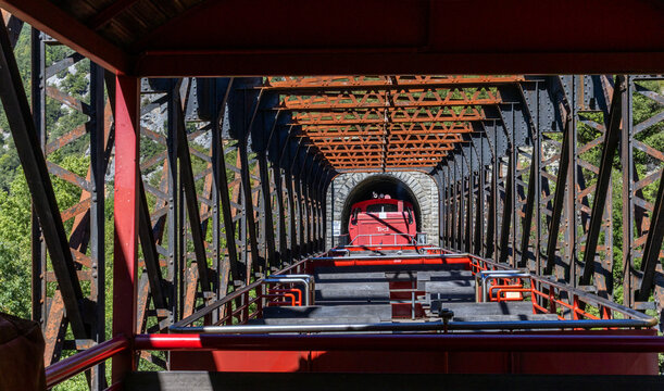 Open tourist train without passengers (Train Rouge) crossing an old truss bridge and entering a tunnel near the village of Axat (Aude, France) in the Pyrenees