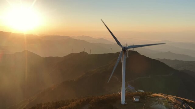 Wind turbine on mountain peak at sunrise with rolling hills and clouds
