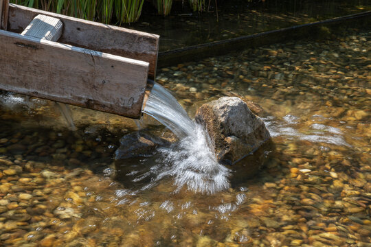 Water flowing in a wooden trough for a therapeutic foot-wading pool with stones.