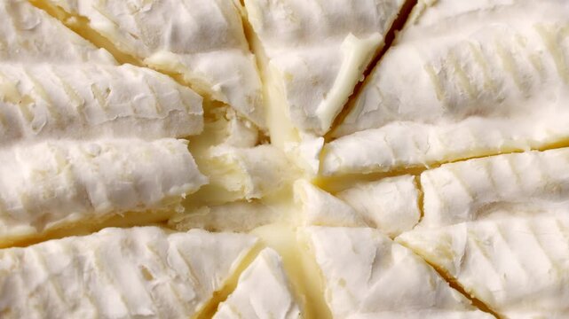 Creamy brie or camembert cheese wheel cut into wedges, soft white rind revealing gooey paleyellow interior circle rotation close up