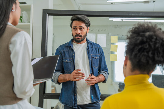 Young businessman explaining project ideas to two attentive female colleagues in modern startup office