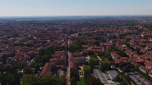 Aerial drone view of Ferrara, Italy, showcasing the historic city center, terracotta rooftops, churches, medieval streets, green spaces, and the Emilia-Romagna cityscape.