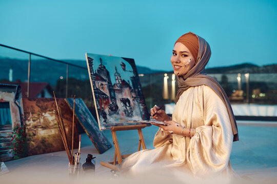 Muslim Woman Artist Painting on Rooftop at Evening Smiling in Hijab and Traditional Dress