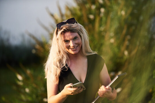 Smiling Blonde Woman With Phone And Tablet Working Outdoors In Casual Business Setting