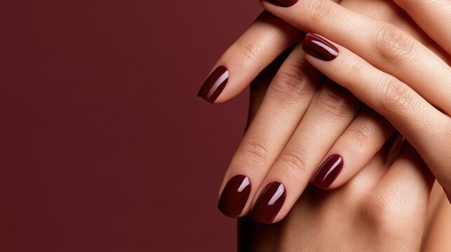 Elegant feminine hands with glossy burgundy manicure against a matching red background