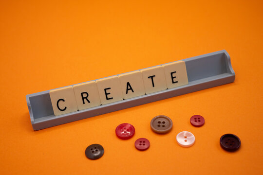 Creative composition on a vibrant orange background showing the word -CREATE- built with board game tiles arranged on a gray base.