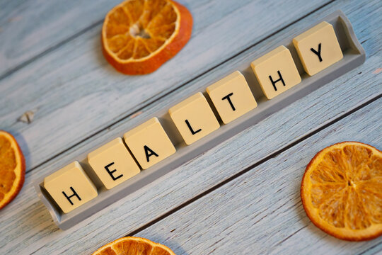 A creative composition featuring the word -Healthy- formed by letter tiles on a blue wooden surface, surrounded by dried orange slices. Concepts of well-being, balanced eating, healthy habits, nutriti