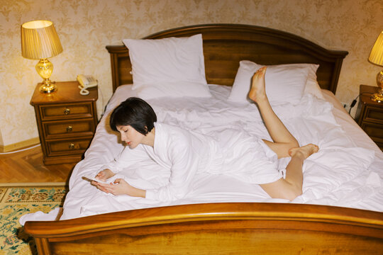 Woman Using Phone in Hotel Room While Lying on Bed