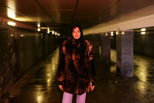 Model Stands in Dark Tunnel Wearing Fur Coat During Nighttime