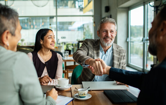 Smiling senior businessman shakes hands during cafe meeting