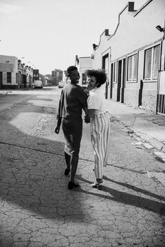 African American women walking down street together with linked arms.