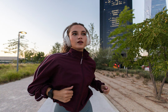 Young woman running urban park listening music