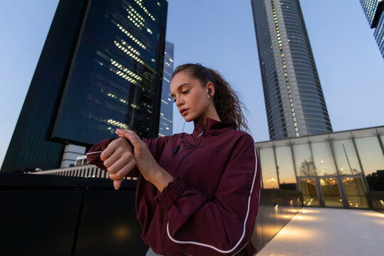 Young woman checking fitness tracker while exercising in urban setting