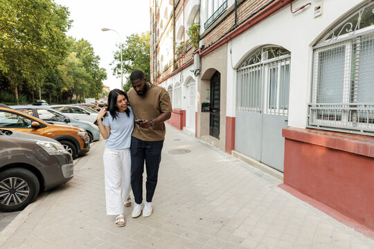 Diverse couple walking outdoors using mobile phone together