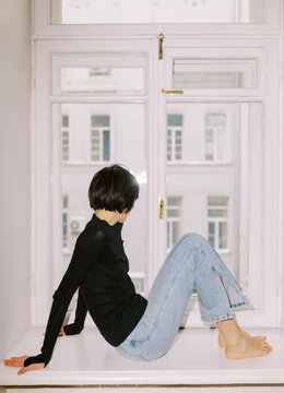 Person Sitting on Window Sill in a City Apartment