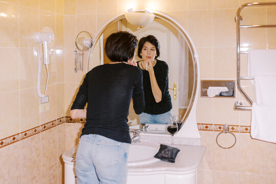 Woman Applying Makeup in Bathroom Mirror During Evening