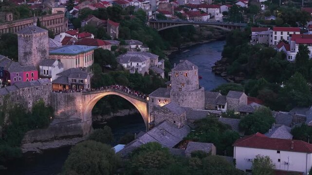 Aerial view of the historic Old Bridge (Stari Most) surrounded by traditional stone buildings, historic towers, and red-roofed houses in the old town at dusk in Mostar, Bosnia and Herzegovina