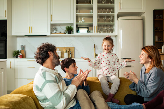 Family applauding daughter performing on sofa in kitchen